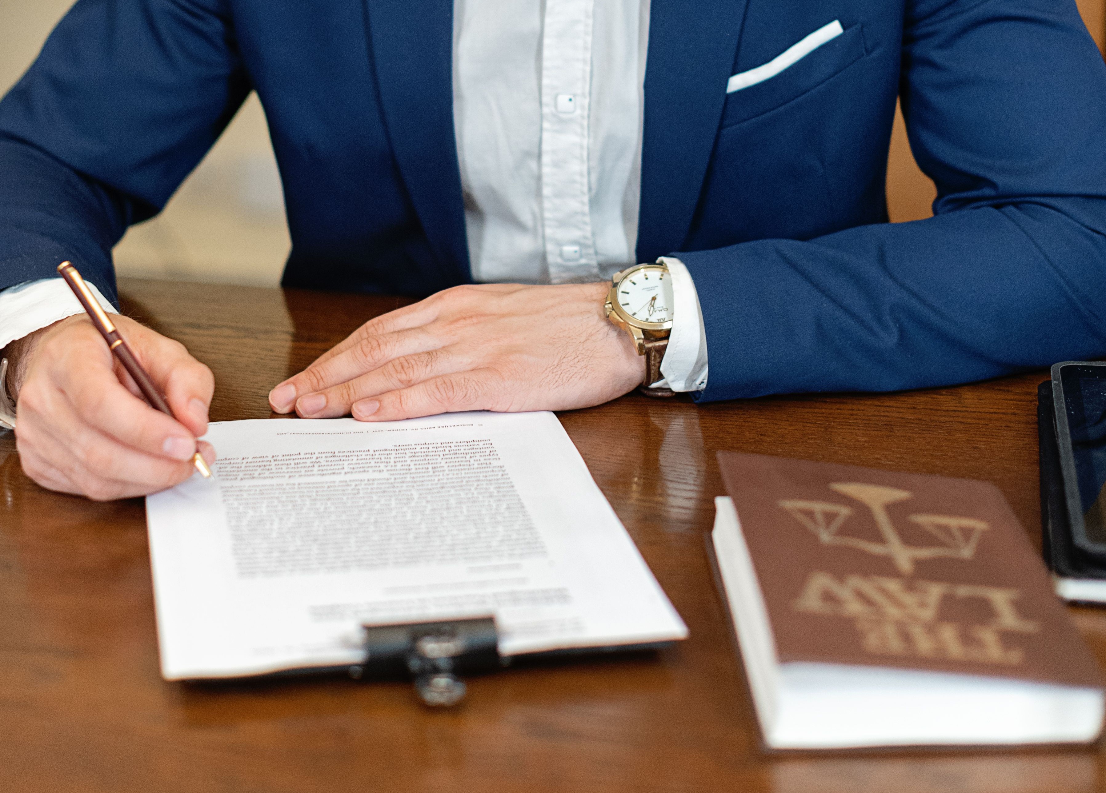 A man in professional attire signs a document on a desk.