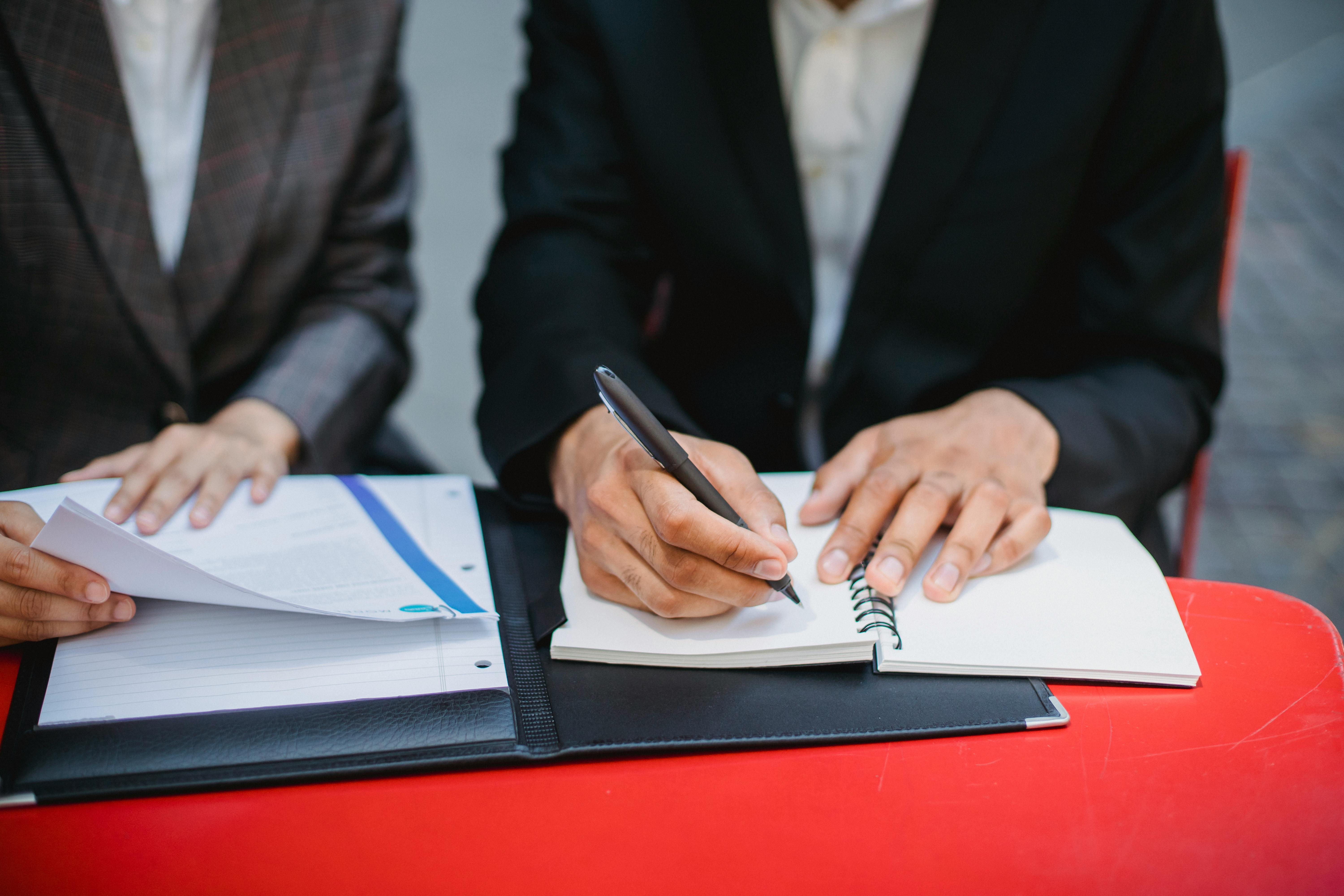 Person in a black suit writing in a notebook