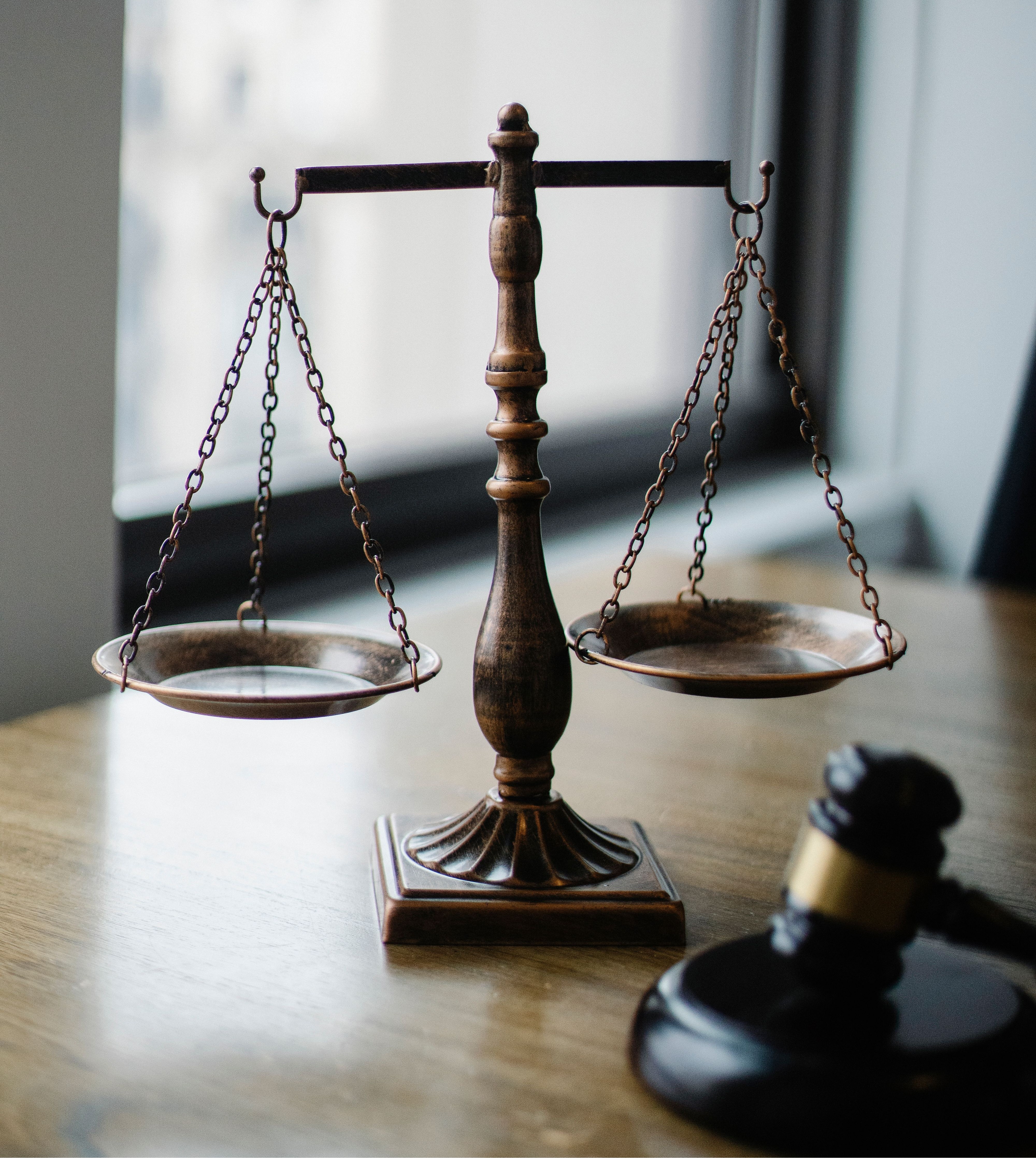A classic scale of justice and gavel on a wooden desk in an office setting.