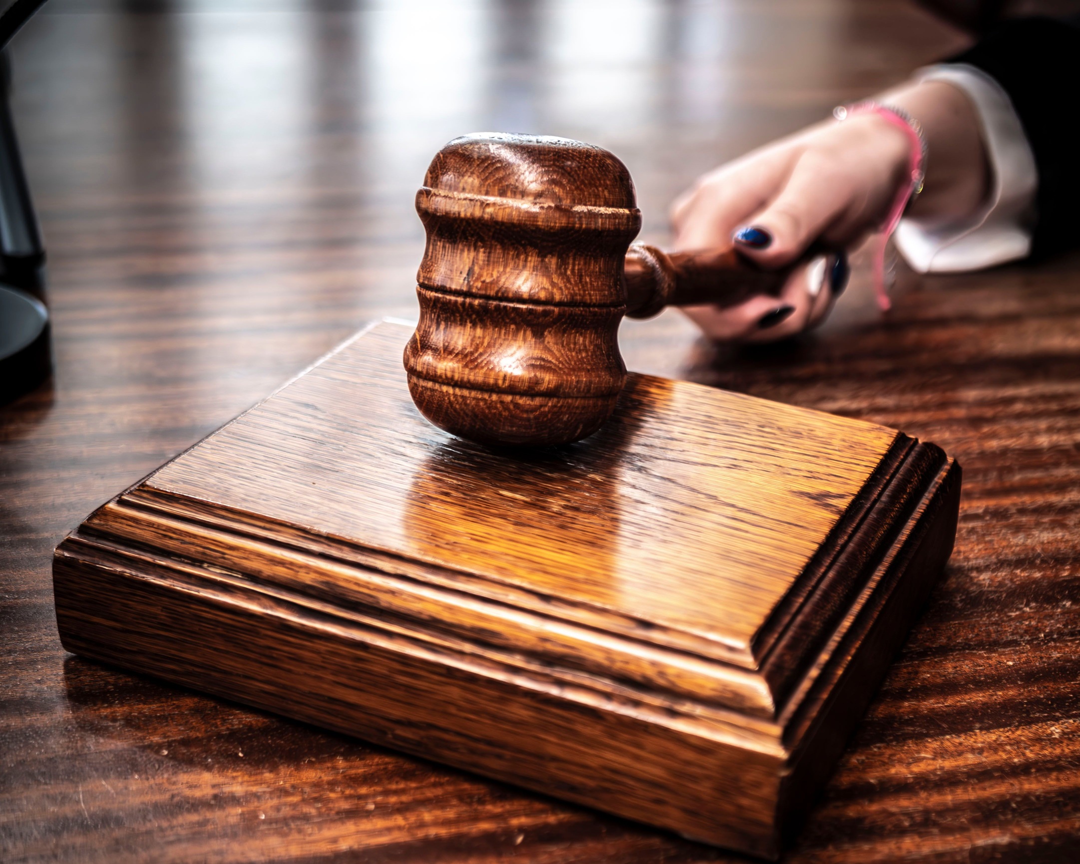 Close-up image of a wooden gavel held by hand on a desk in a courtroom setting.