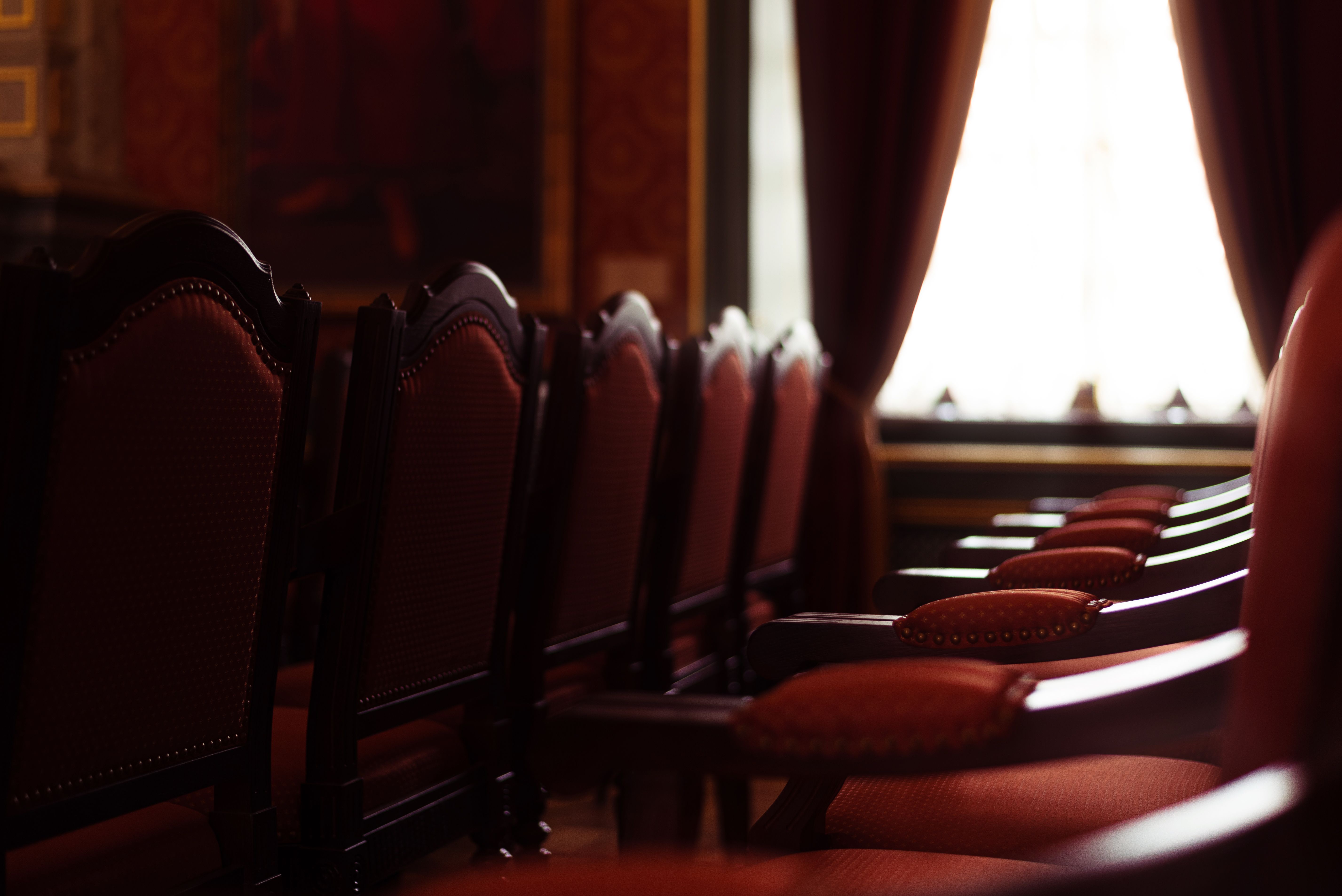 A row of elegant empty chairs in a dimly lit vintage room with red curtains